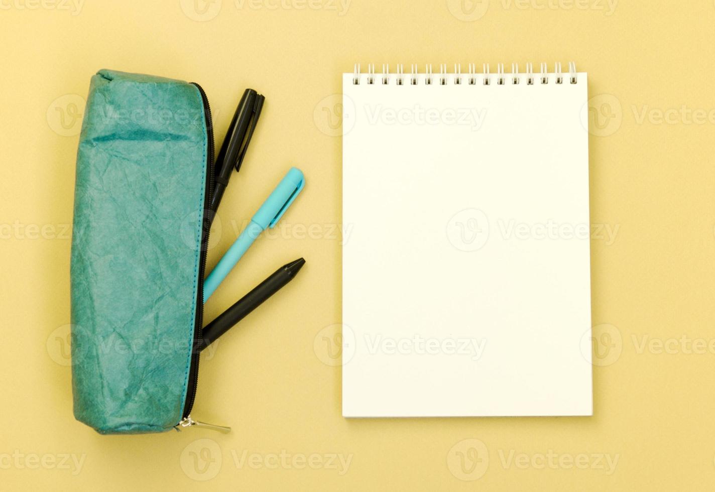 ovanifrån av ett skrivbord med pennfodral och ett tomt anteckningsblock på gul bakgrund. platt läggning av föremål med plats för text. foto