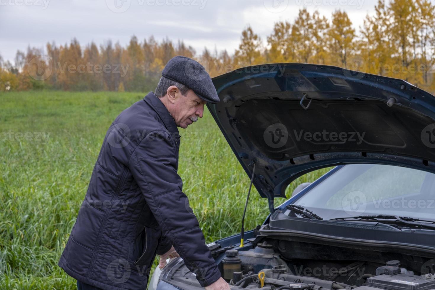 äldre pensionerad man öppnar huven på sin bil och tittar in i motorn foto