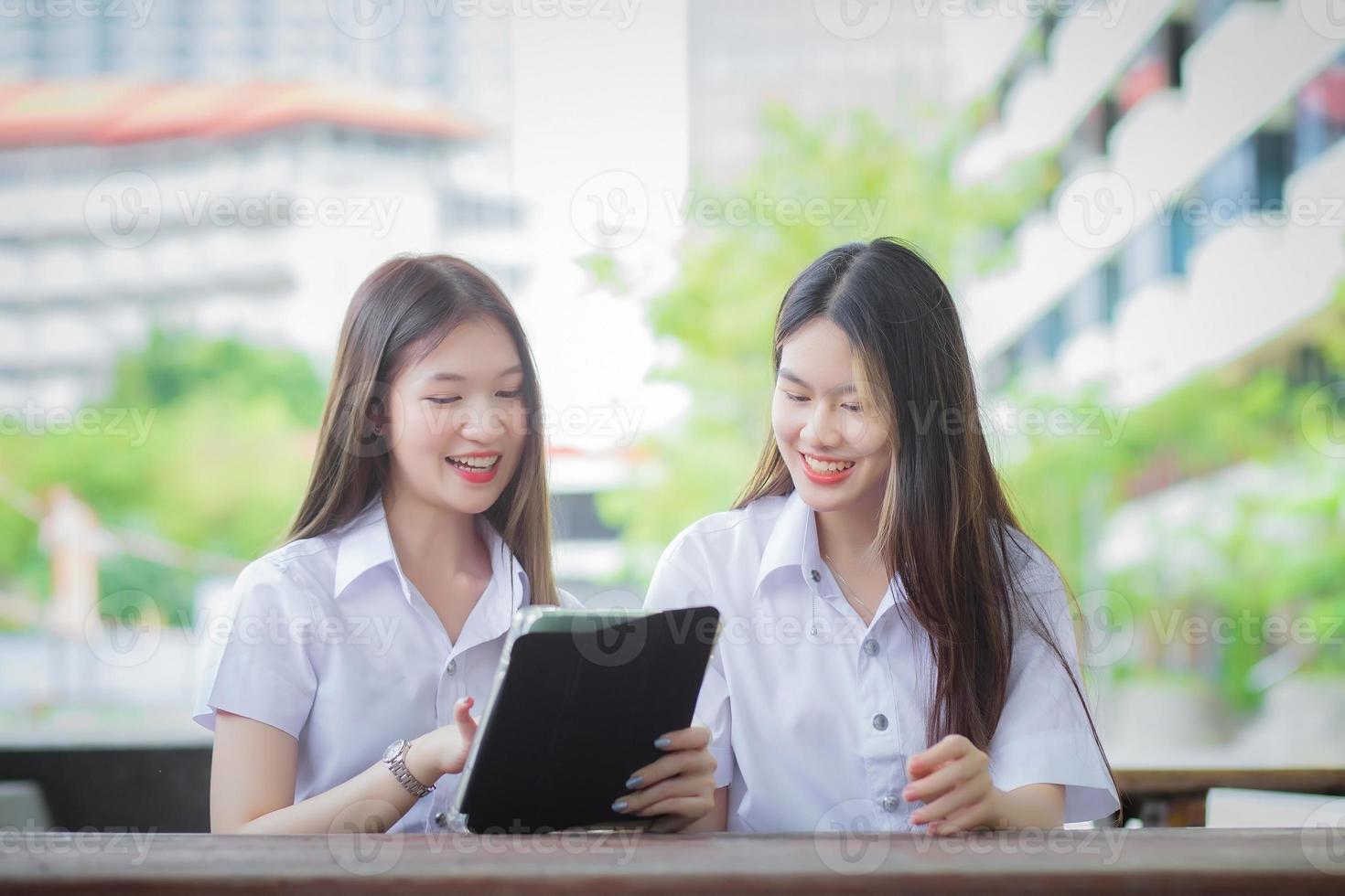 två unga asiatiska flickstudenter rådgör tillsammans och använder en surfplatta för att söka information till en studierapport. foto