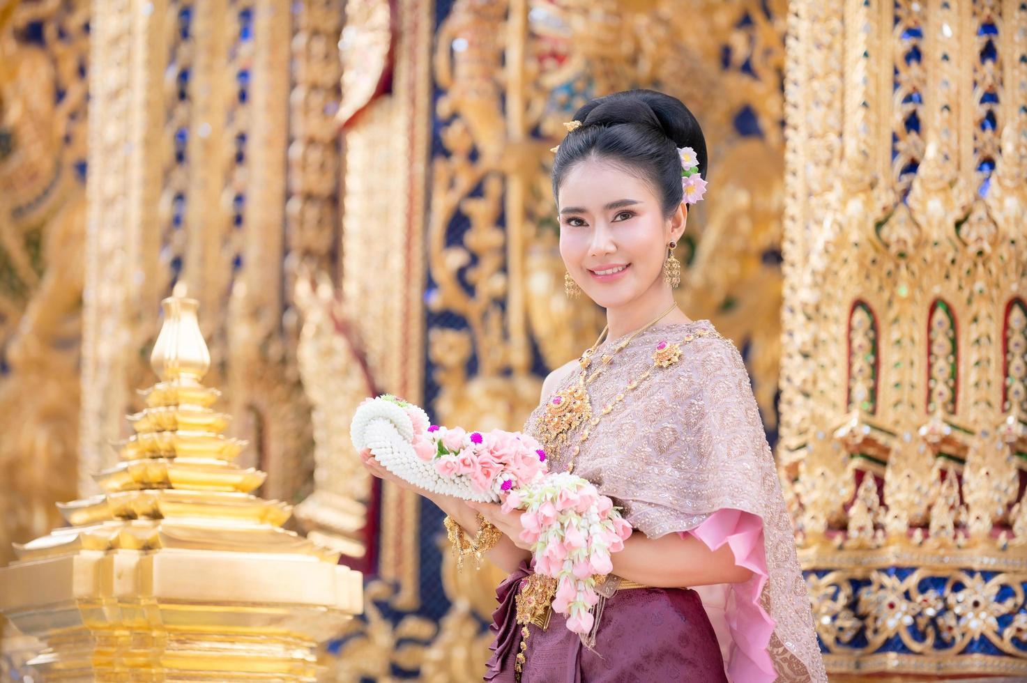 en vacker elegant thailändsk kvinna i thailändsk klänning prydd med dyrbara smycken står som håller i en blomstergirlang foto