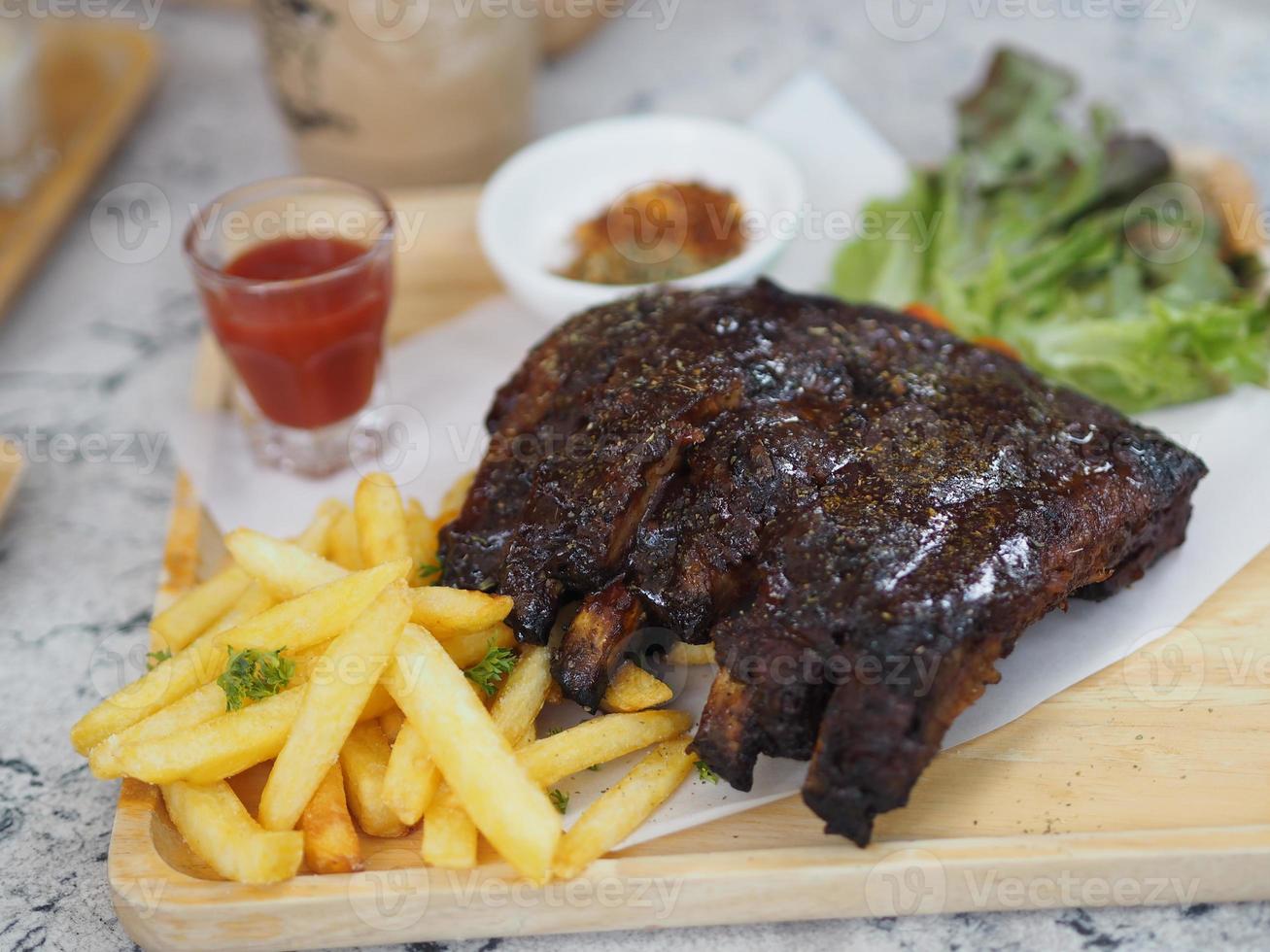 fläsk spareribs bbq, grillad fläsk revben med pommes frites grönsakssallad, tomatsås i ett klart glas på träbricka, mat foto