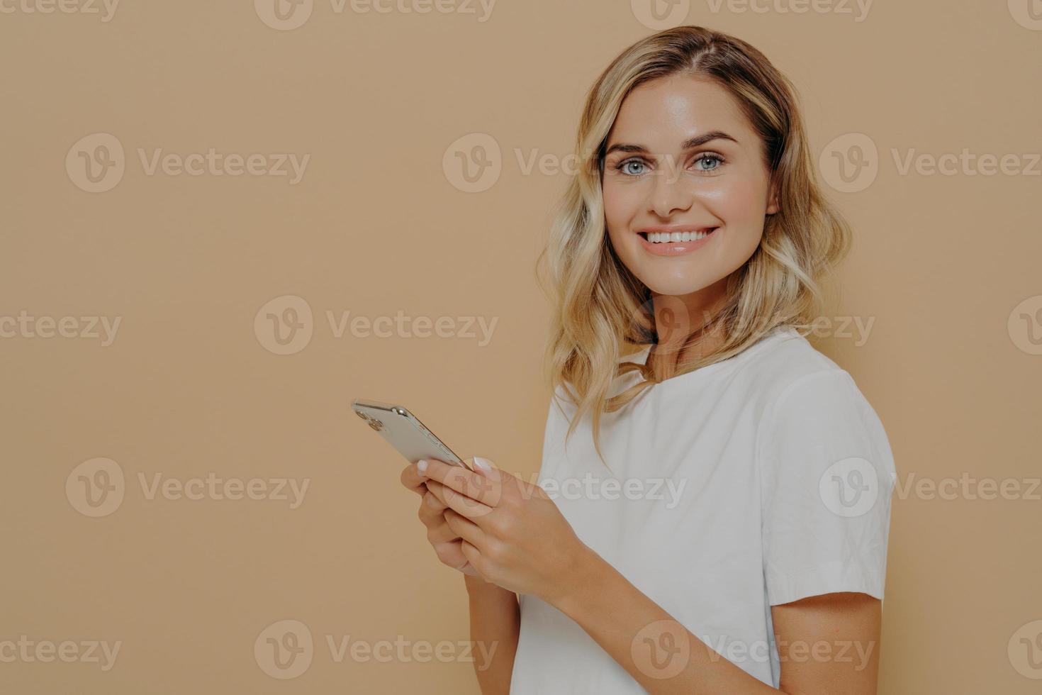 porträtt av glad ung kvinna i vit t-shirt som är glad över att läsa goda nyheter på smartphone foto