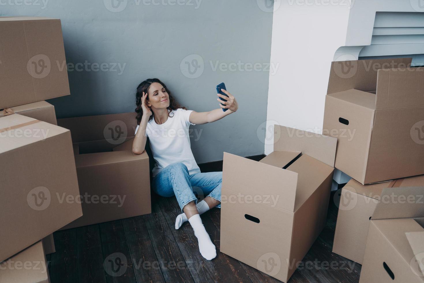 glad kvinna packar upp lådor och tar selfie i en ny lyxig lägenhet. framgång koncept. foto