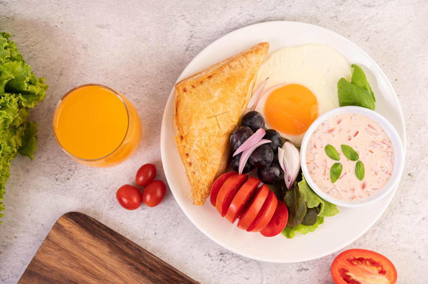 Frukosten består av bröd, stekt ägg, salladsdressing, svarta druvor, tomater och skiva. foto