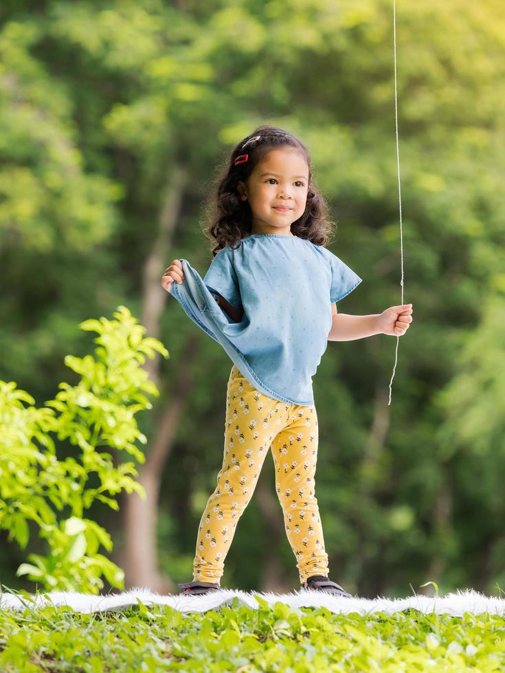 asiatisk liten flicka som står på mattan, leker och lär sig utanför skolan för att njuta i naturparken foto