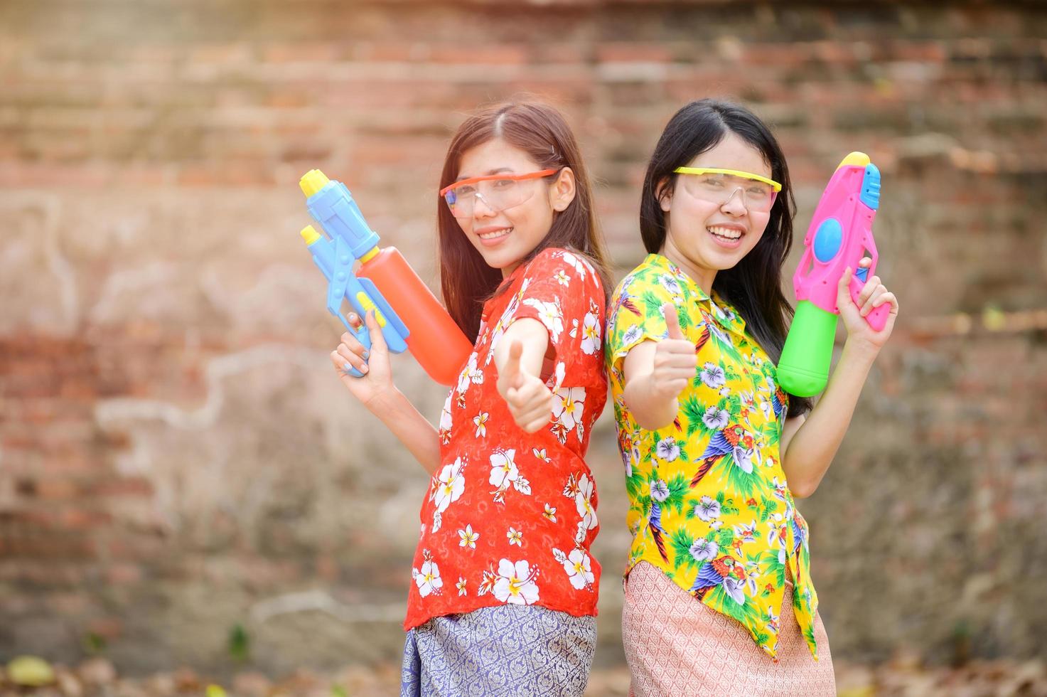 vackra asiatiska kvinnor håller plastvattenpistoler vid ett gammalt tempel under songkran, den vackraste och roligaste vattenfestivalen i thailand foto