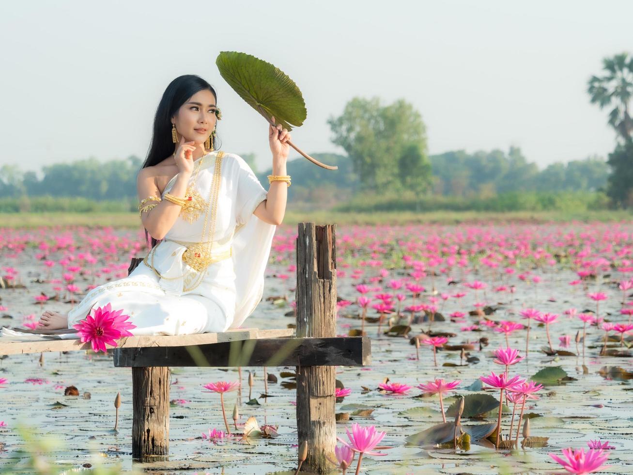 en elegant thailändsk kvinna som bär traditionella thailändska kläder bär lotusblommor blad som samlats in från ett lotusfält foto