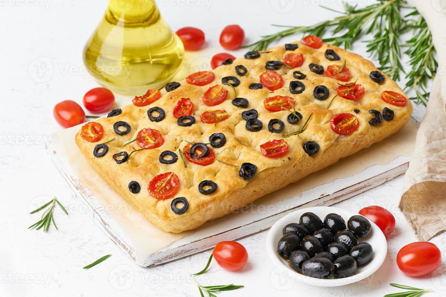 focaccia med tomater, oliver och rosmarin. hela italienska plattbröd, flaska med olja foto