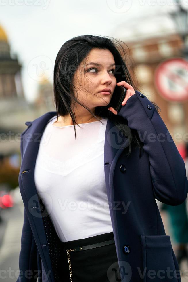 kvinna med långt hår pratar i telefon. höst eller vinter, flicka i utomhus. vacker intelligent brunett på gatan i Saint-Petersburg i centrum, kopieringsutrymme foto