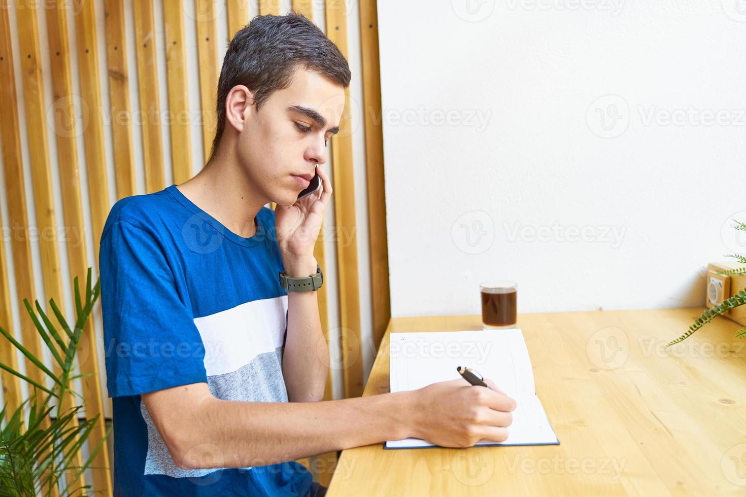 ung man skriver information till anteckningsblock och talar mobiltelefon, tonåring i vardagskläder planerar ett schema foto