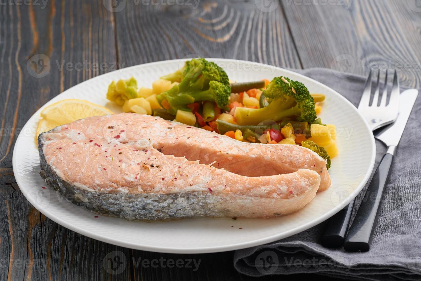 ånga lax och grönsaker, hälsosam kost. vit platta på rustikt träbord, sidovy foto