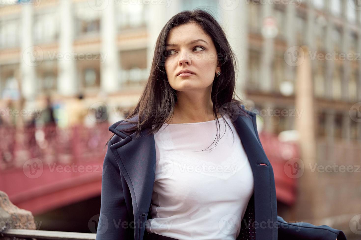 vacker allvarlig smart brunett flicka står på bron på gatan i st. petersburg i stadens centrum. en charmig eftertänksam modeklädd kvinna med långt mörkt hår tittar bort foto