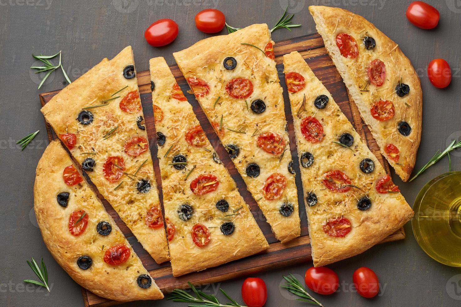focaccia, pizza, italienskt platt bröd med tomater, oliver och rosmarin på mörkbrunt bord foto