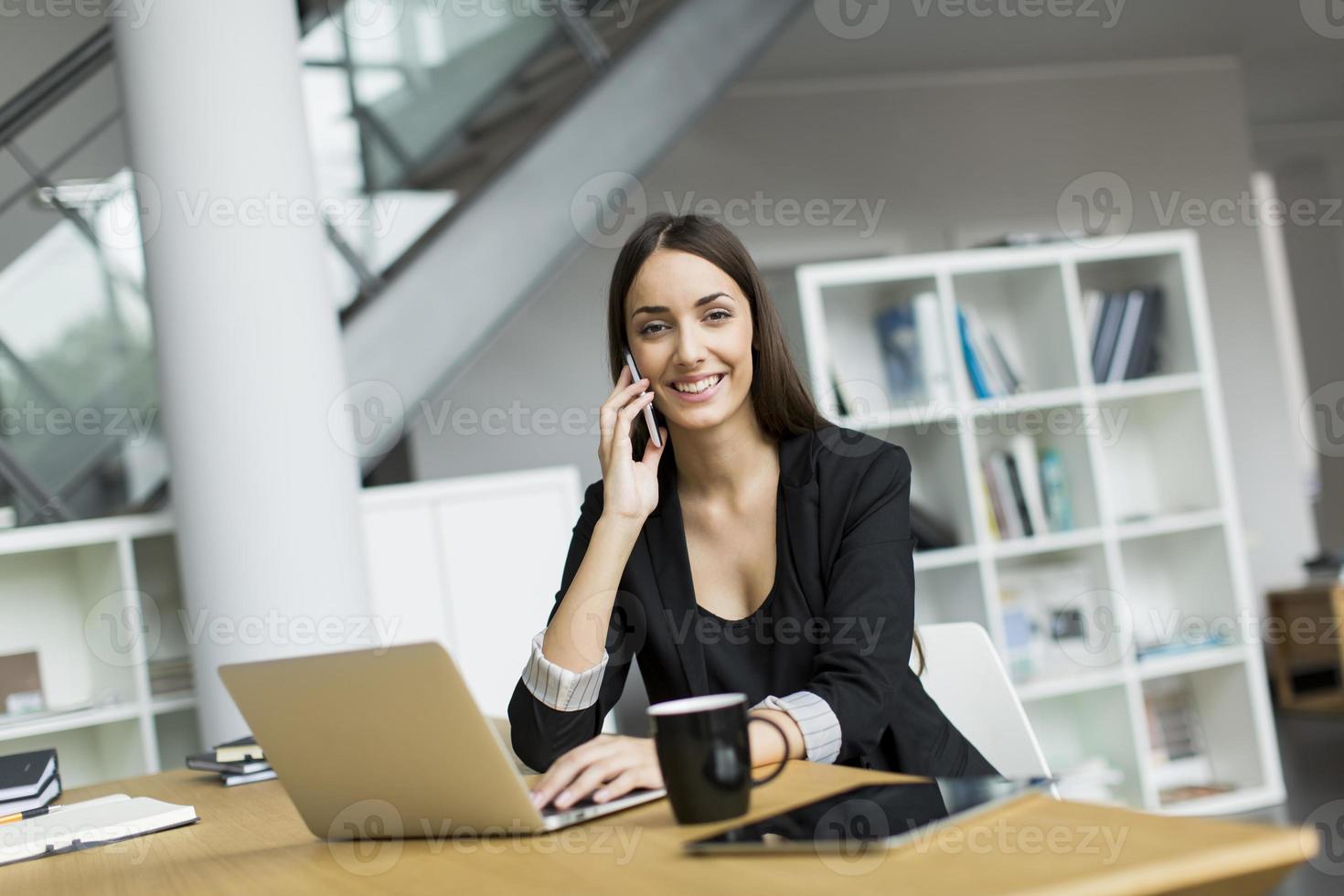 le ung kvinna med laptop och mobiltelefon på ett kontor foto