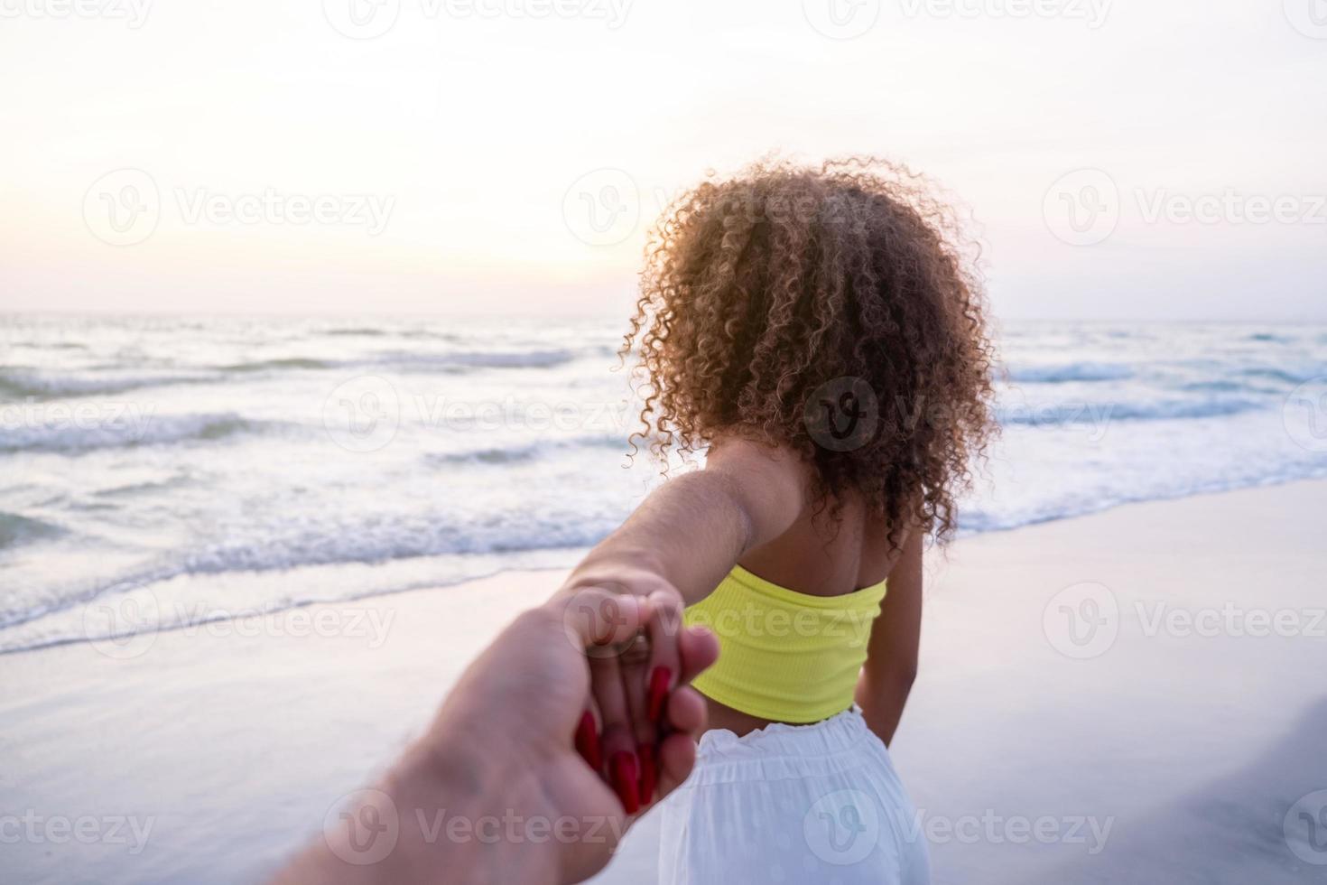 flicka håller manlig hand och springer på tropiska exotiska stranden till havet. följ mig skott av ung kvinna dra sin pojkvän på stranden. sommarlov eller semester. pov. foto