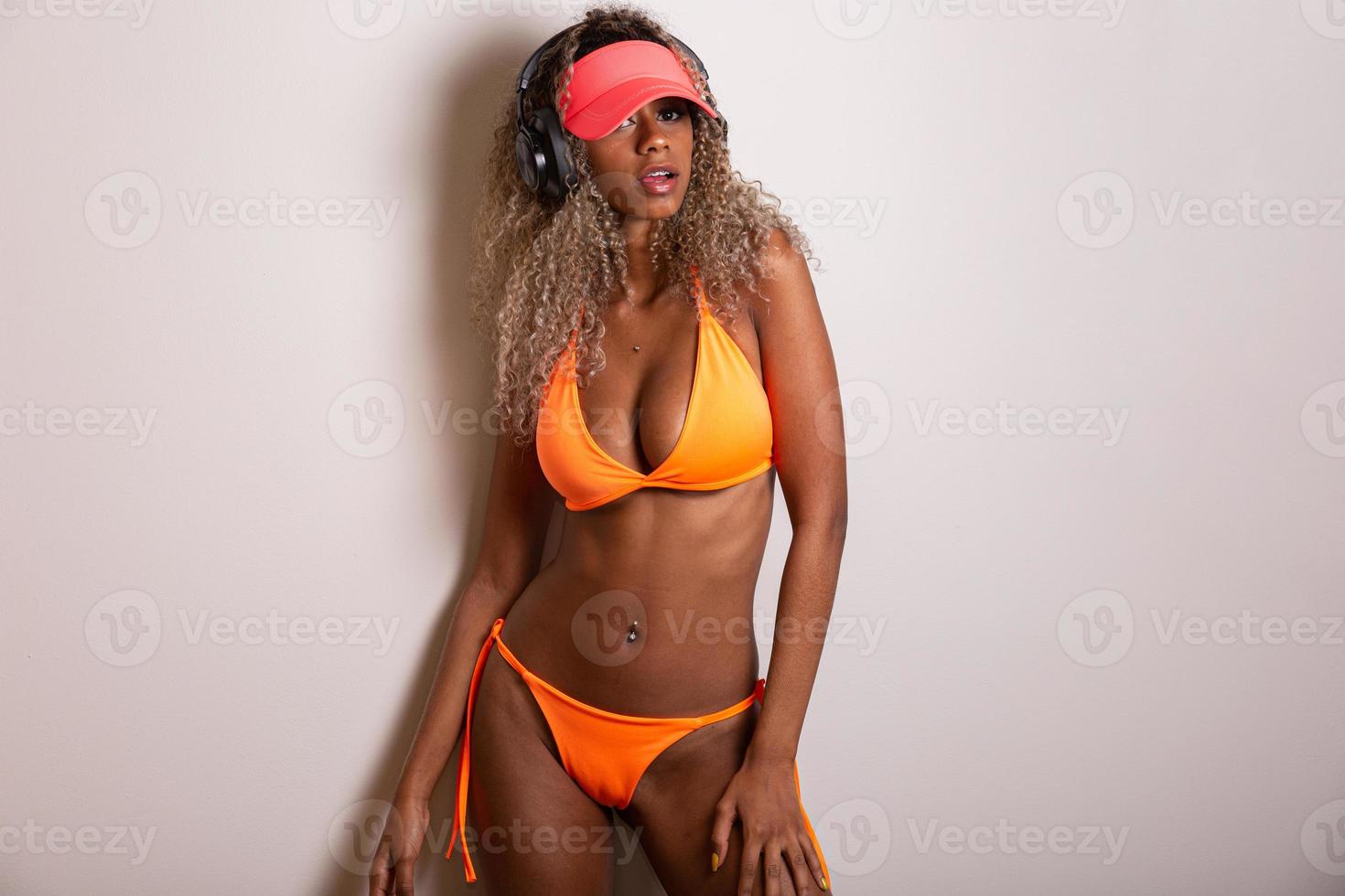 attraktiv lockigt hår flicka i en orange bikini, hatt, känslomässigt öppnad mun på en vit bakgrund med en perfekt kropp. isolerat. studio skott. foto