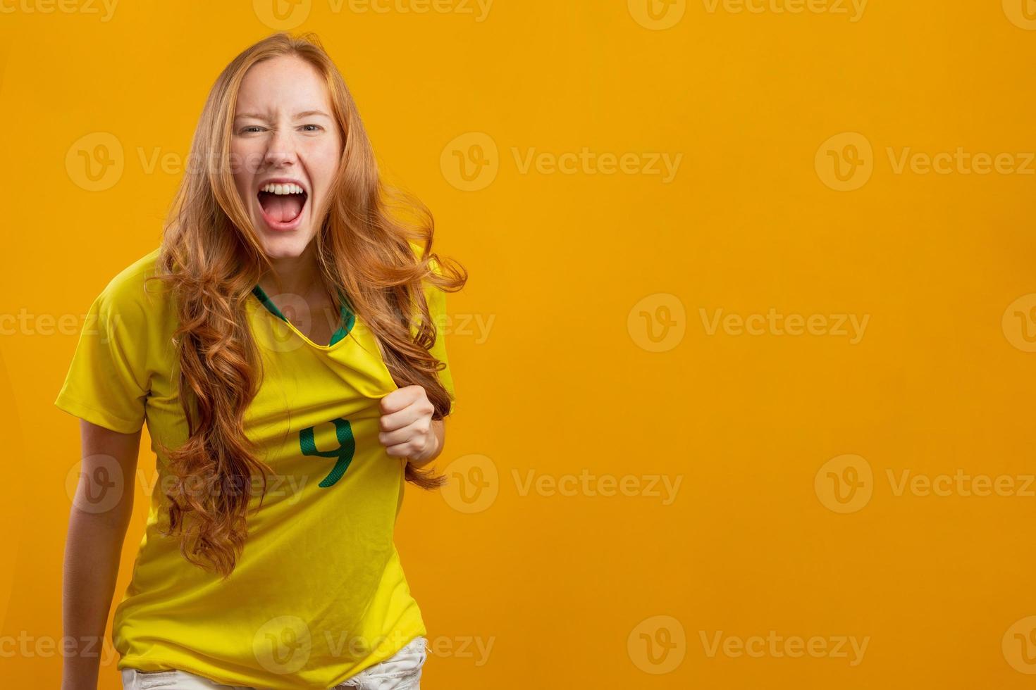 brasiliens anhängare. brasiliansk rödhårig kvinna fan firar på fotboll, fotbollsmatch på gul bakgrund. brasilianska färger. foto