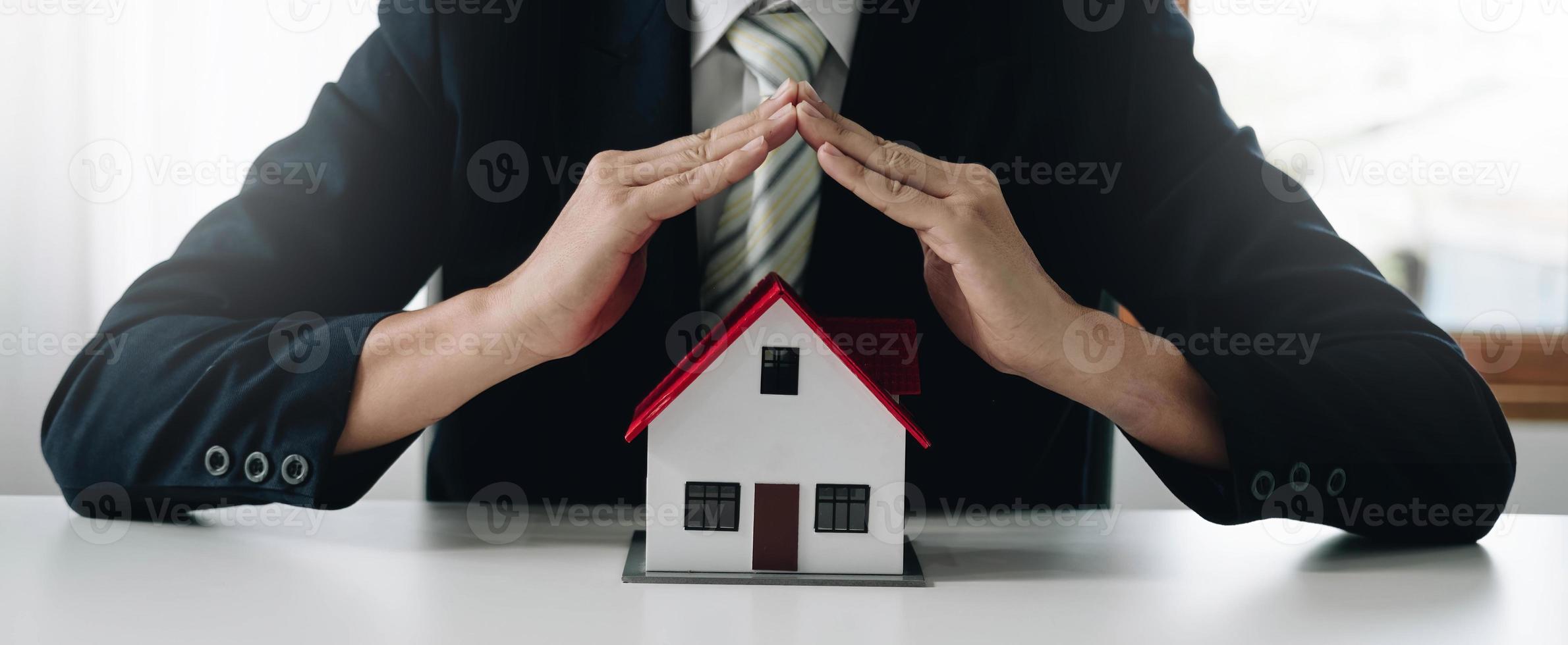 ett litet grått modellhus är ett exempel på ett hem i ett bostadsprojekt, en försäkringssäljare gör en symbolisk hemskyddshandling inom hemförsäkringen. fastighetsleasing koncept. foto
