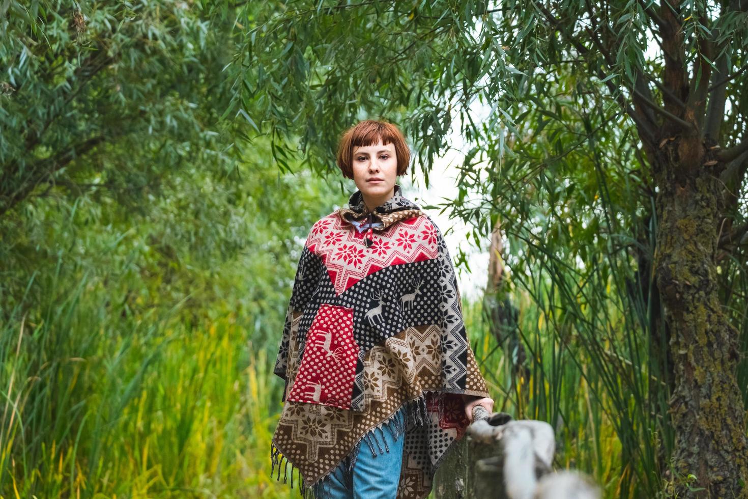 ung kvinna resenär klädd i en poncho promenad utomhus i höst fält foto