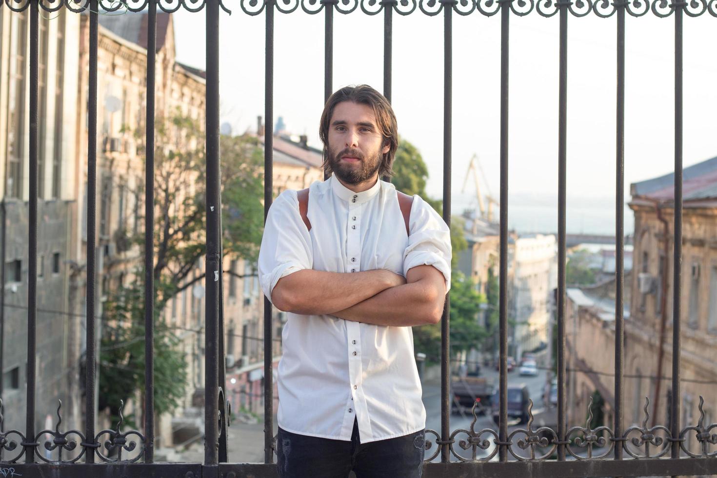 porträtt av skäggig man i vit skjorta, urban bakgrund, hipster poserar på bron foto