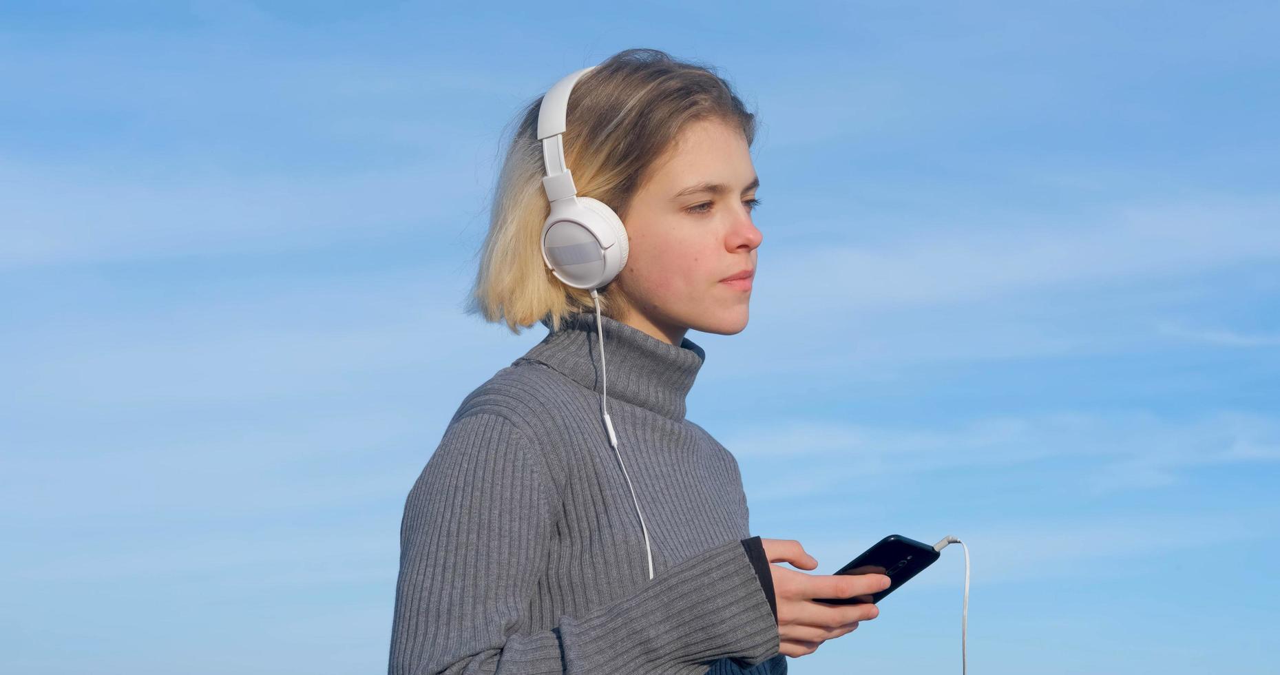ung stilig kvinna lyssna på musik med hörlurar utomhus på stranden mot solig blå himmel foto