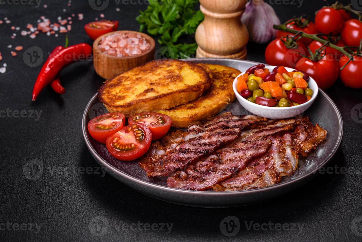 skivor av utsökt grillat bacon med krutonger stekt i ägg med kryddor, salt, grönsaker och örter foto