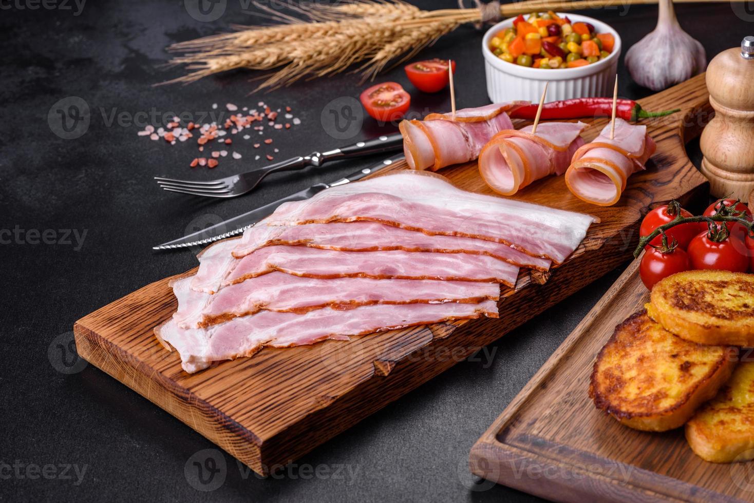 skivor av utsökt rå eller saltad bacon med kryddor, salt, grönsaker och örter på en träskärbräda foto