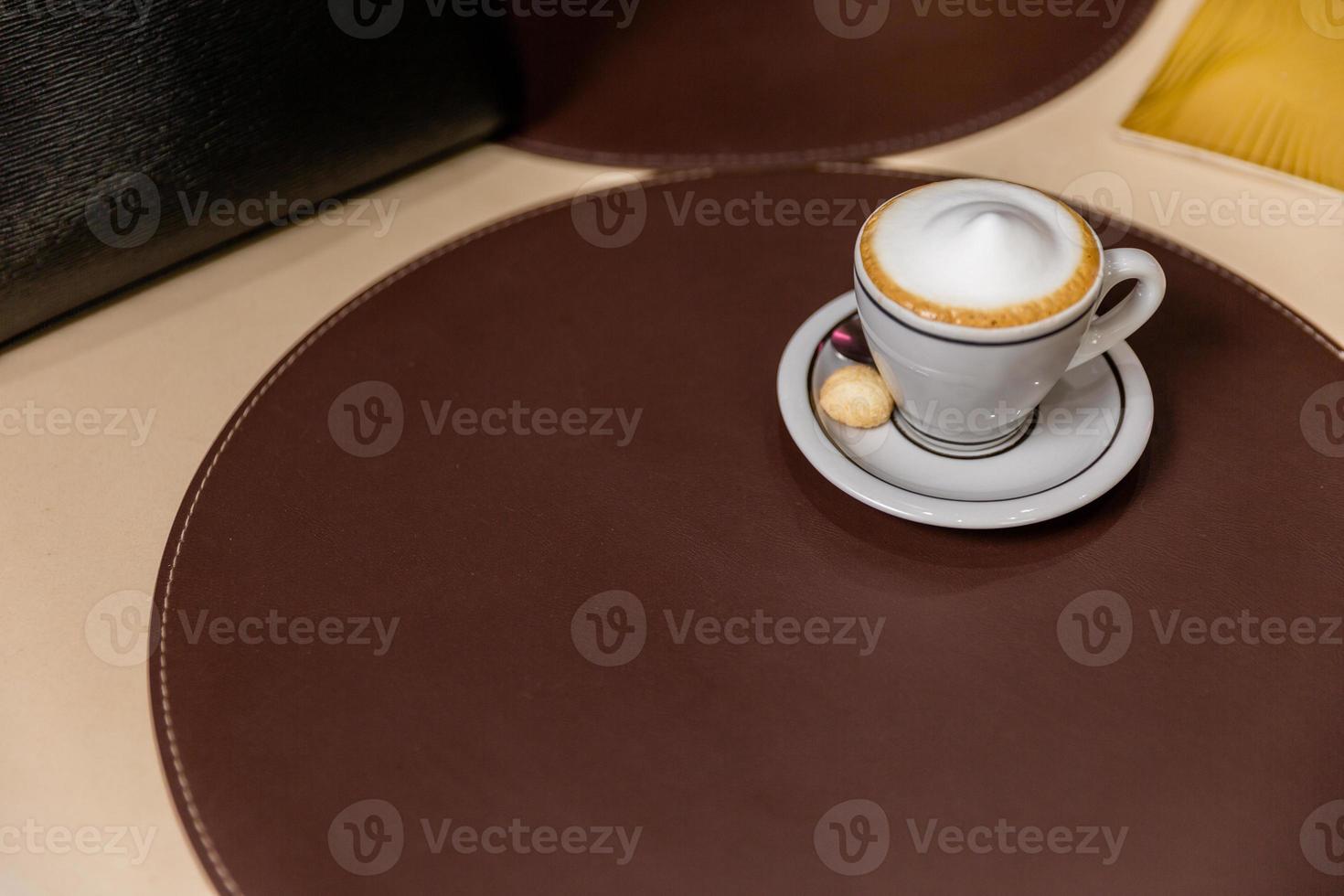 cappuccino med fint skummande skum. latte art med ett hjärta tillverkat av mjölk. kaffekopp med ett fat och en tesked på ett bord. foto