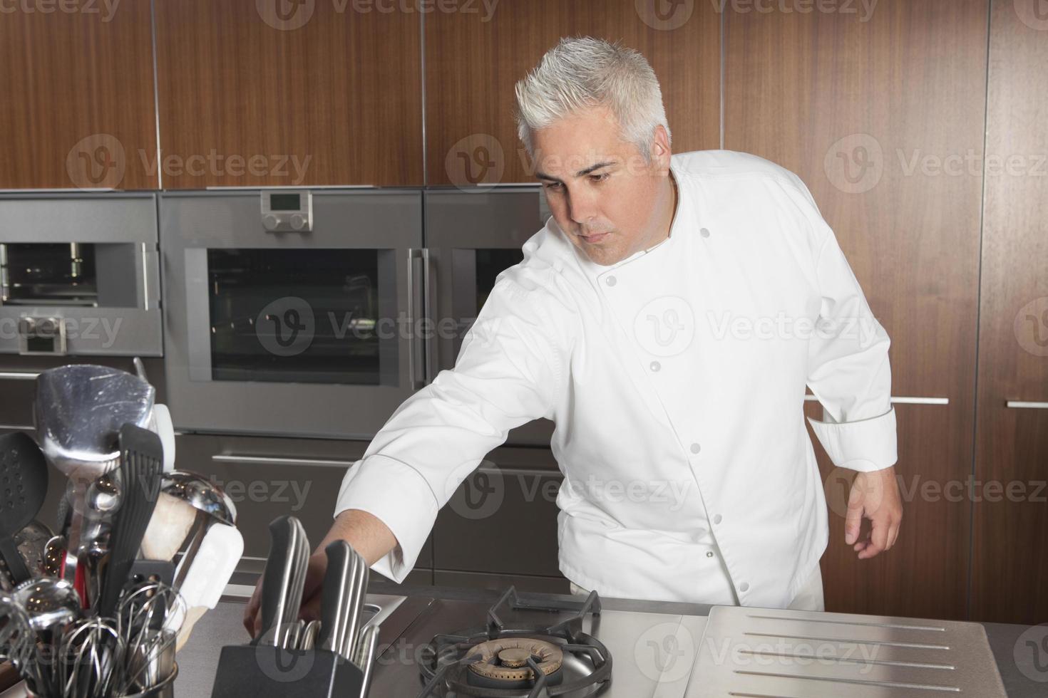 kocken lutar sig för kniven i det kommersiella köket foto