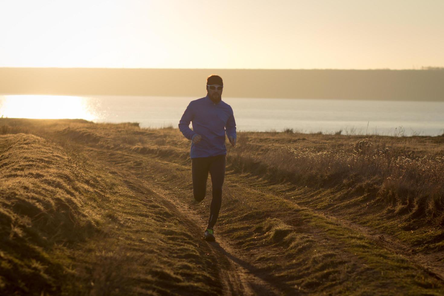 ung man trail runner utbildning utomhus på fälten, solnedgång i sjön bakgrund foto
