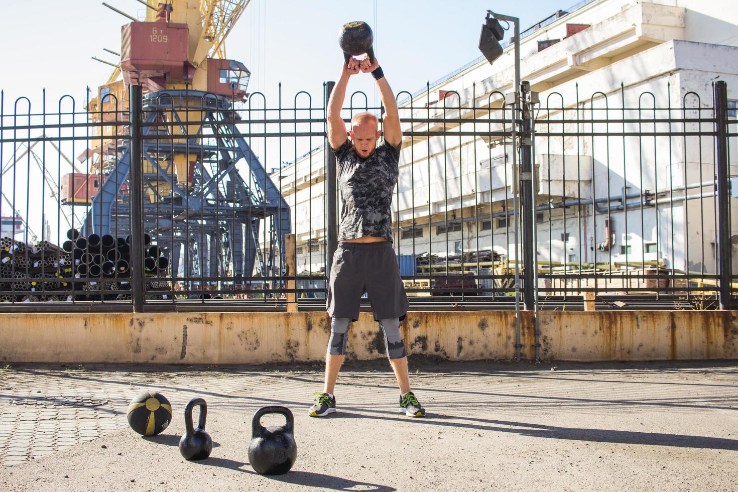 ung skäggig manlig idrottare tränar i industrizon i solig dag, kettlebellsövningar utomhus, urban bakgrund foto