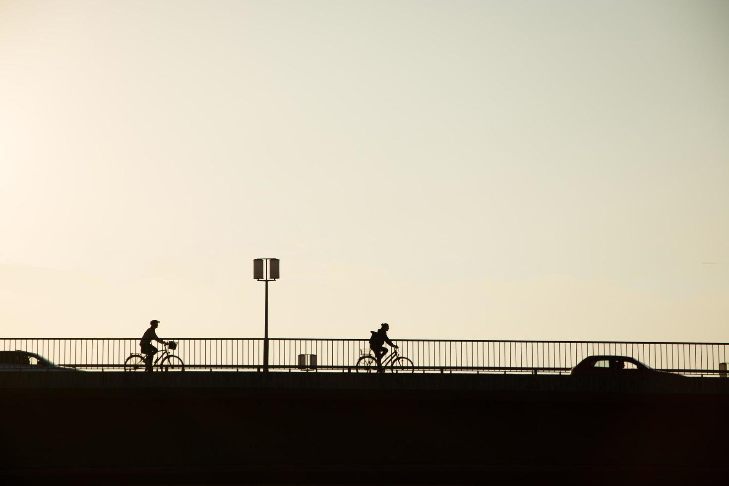 siluett cykel av cykel ryttare på bron mot solnedgången, minimalistisk stadslandskap foto