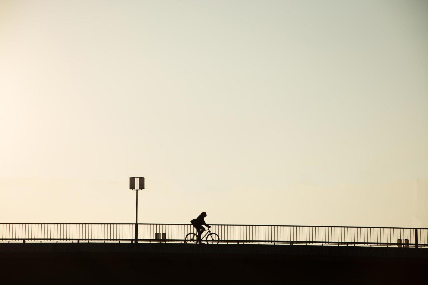 siluett cykel av cykel ryttare på bron mot solnedgången, minimalistisk stadslandskap foto