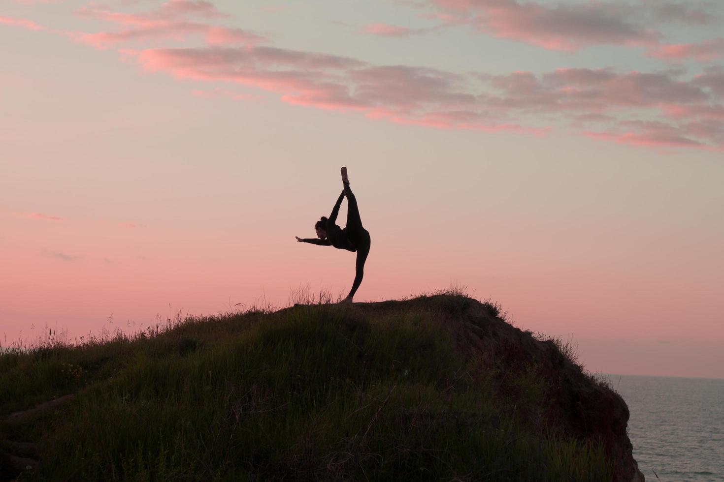 vältränad kvinna gör yoga stretching övning utomhus i vackra bergslandskap. hona på klippan med hav och soluppgång eller solnedgång bakgrund utbildning asans. siluett av kvinna i yogaställningar foto