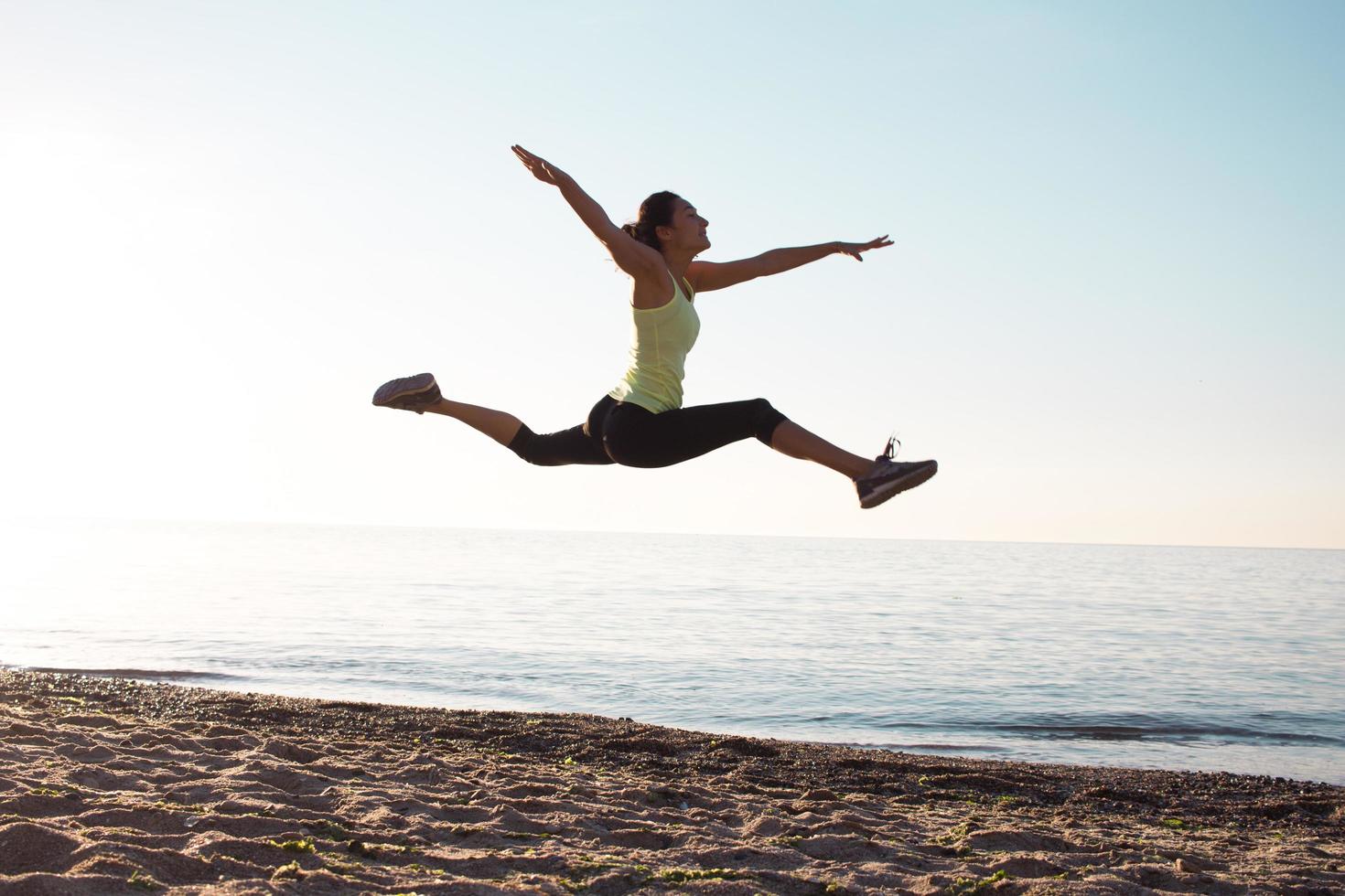 ung professionell gymnastkvinna dansar på stranden, träningsövningar med coola junps, soluppgång i havet eller havets bakgrund foto