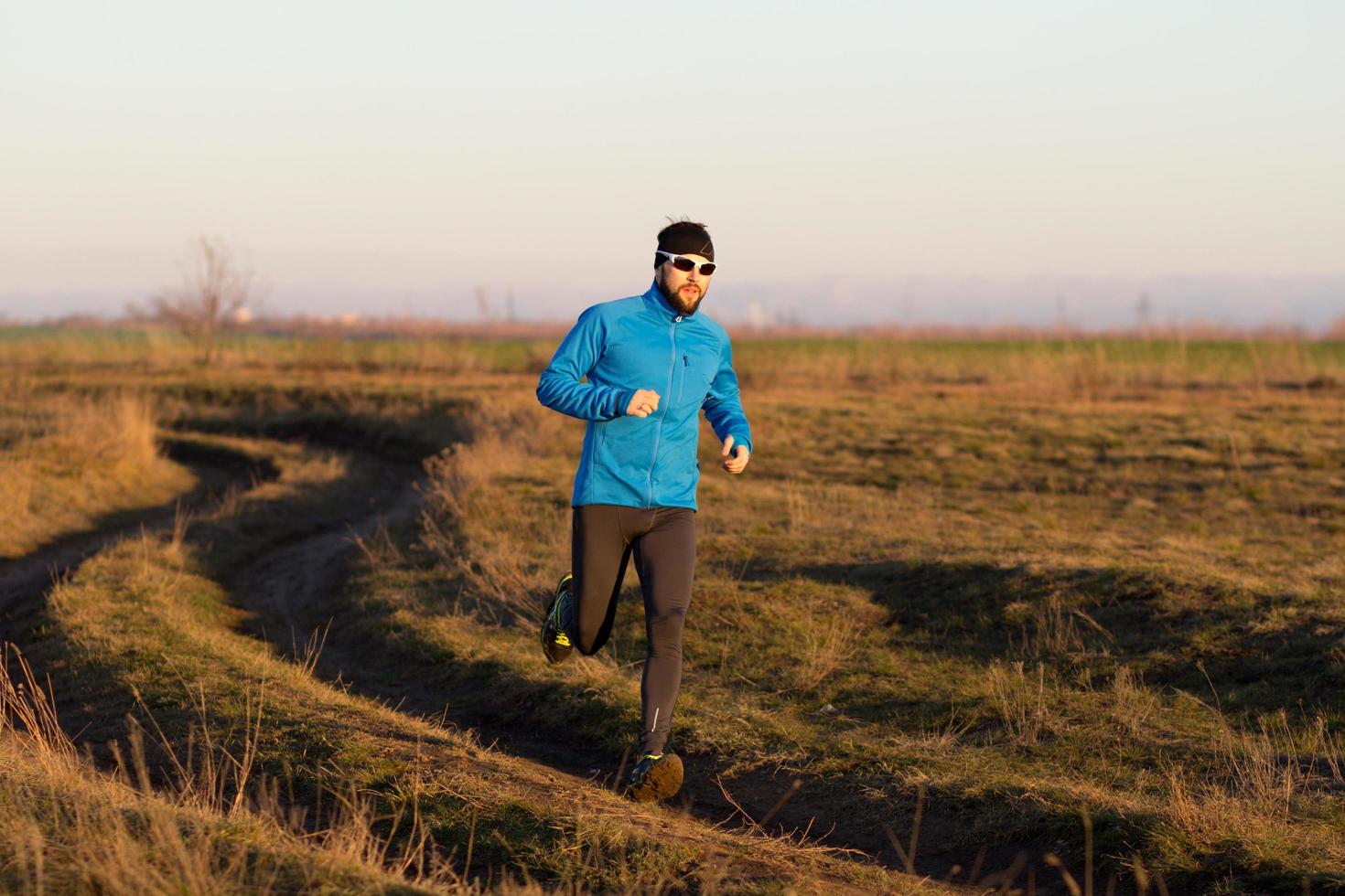 ung man trail runner utbildning utomhus på fälten, solnedgång i sjön bakgrund foto