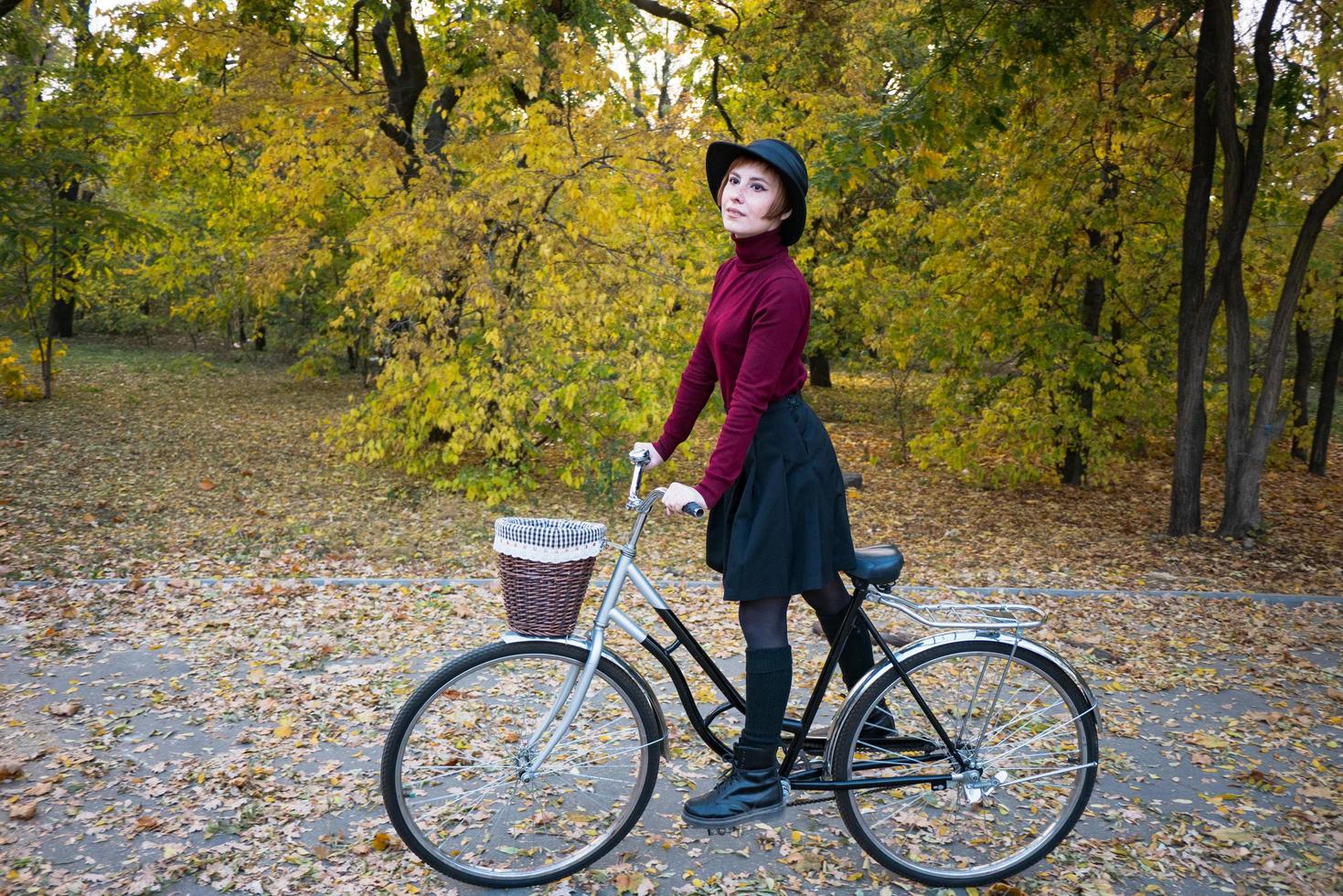 ung kvinna i höstparken läsa bok, vacker rödhårig kvinna med cykel på det gröna gräset foto