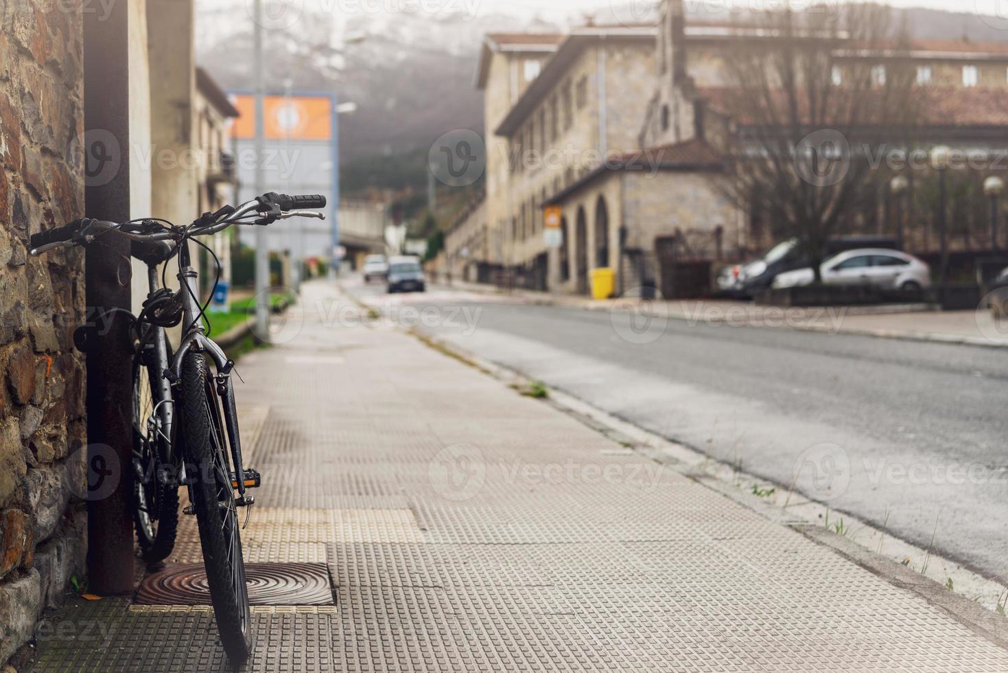 cykel parkerad på trottoaren nära stadsgatan i Spanien. cykel luta på stolpen bredvid gamla byggnaden. framifrån av cykel på suddig byggnad, bilkörning på vägen och bergsbakgrund. europa resor. foto