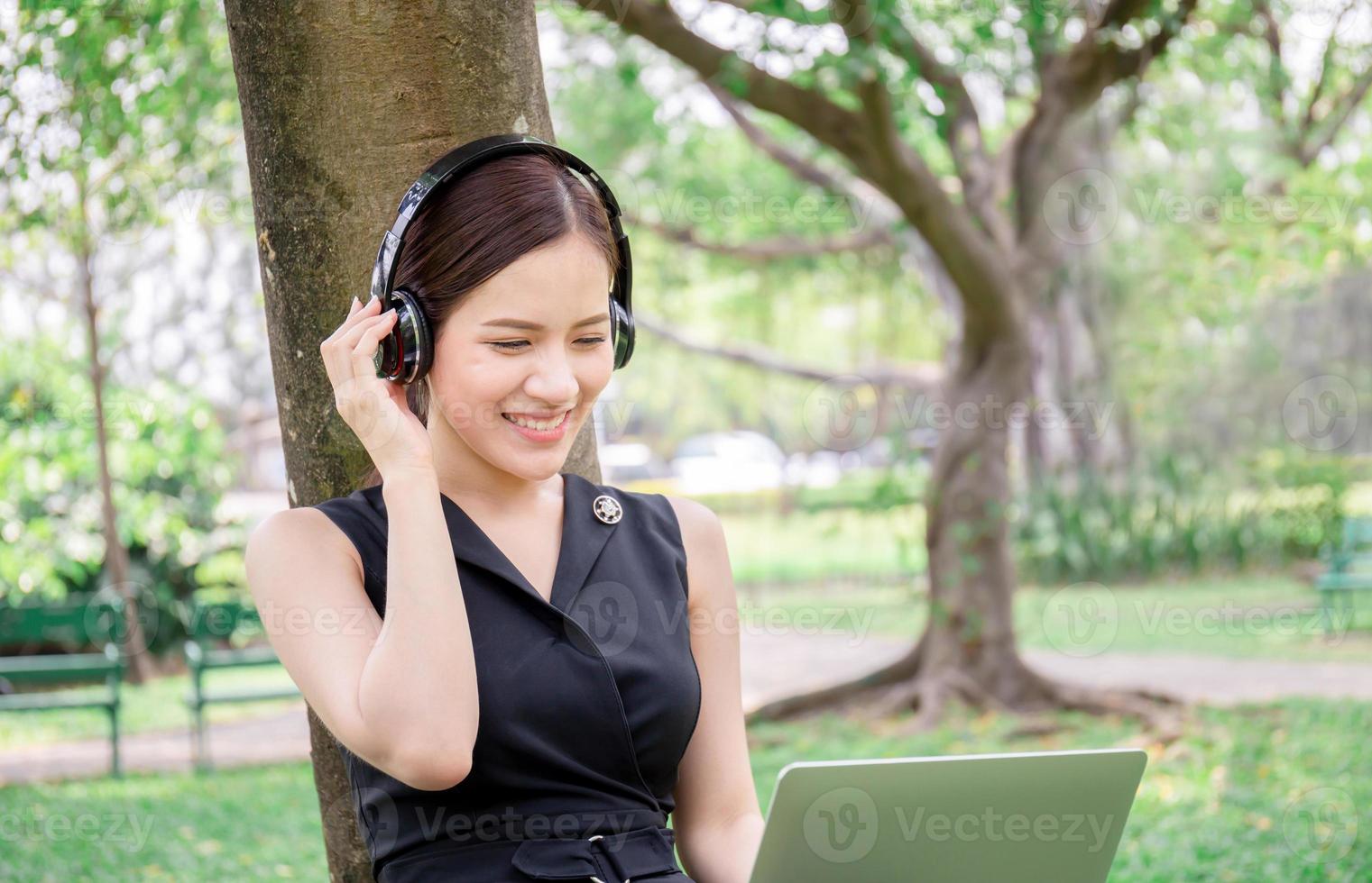 vacker ung kvinna med hörlurar och laptop njuter och avslappnad i musik i parken foto