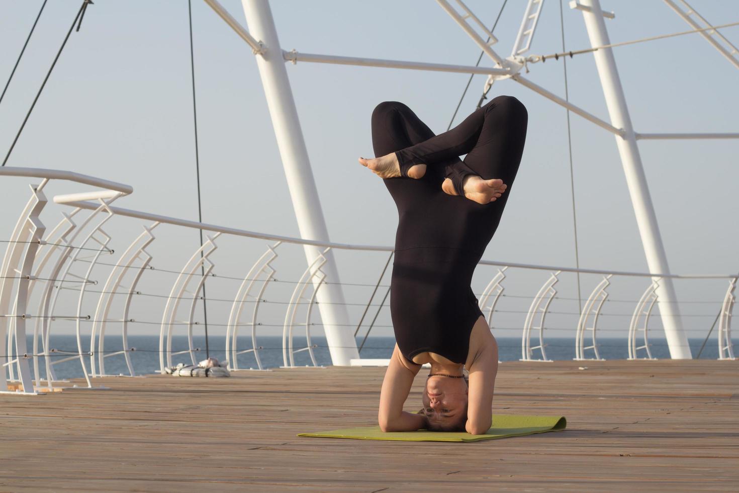 flicka i svarta sportkläder utövar yoga på träpiren morgon havet på bakgrunden foto