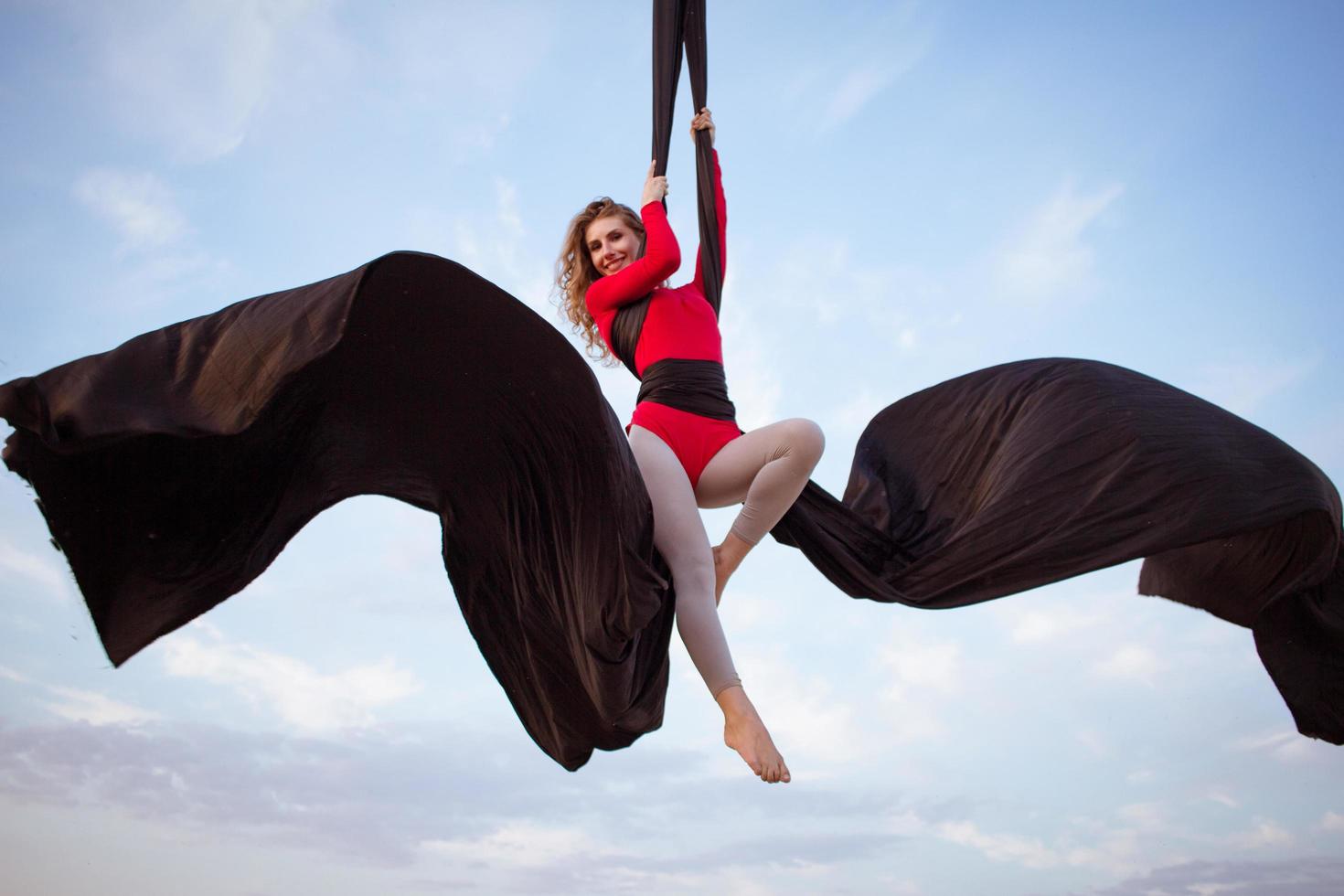 övningar med antenn silke utomhus, himmel bakgrund. vacker passform kvinna träning akrobatisk i luften. foto