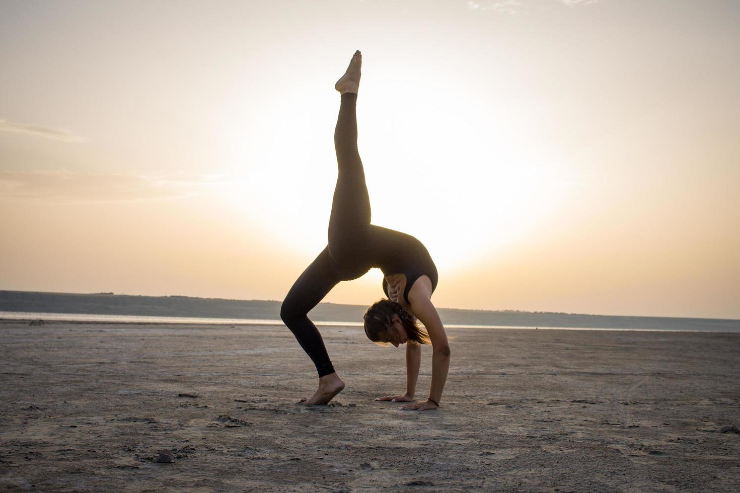 ung vältränad kvinna som tränar yogaställningar i öknen under solnedgången eller soluppgången, kvinna i svarta sportkläder gör stretchövningar foto