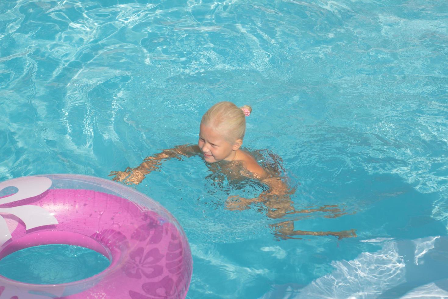blond unge har bra tid i poolen, liten flicka simmar på sommaren foto