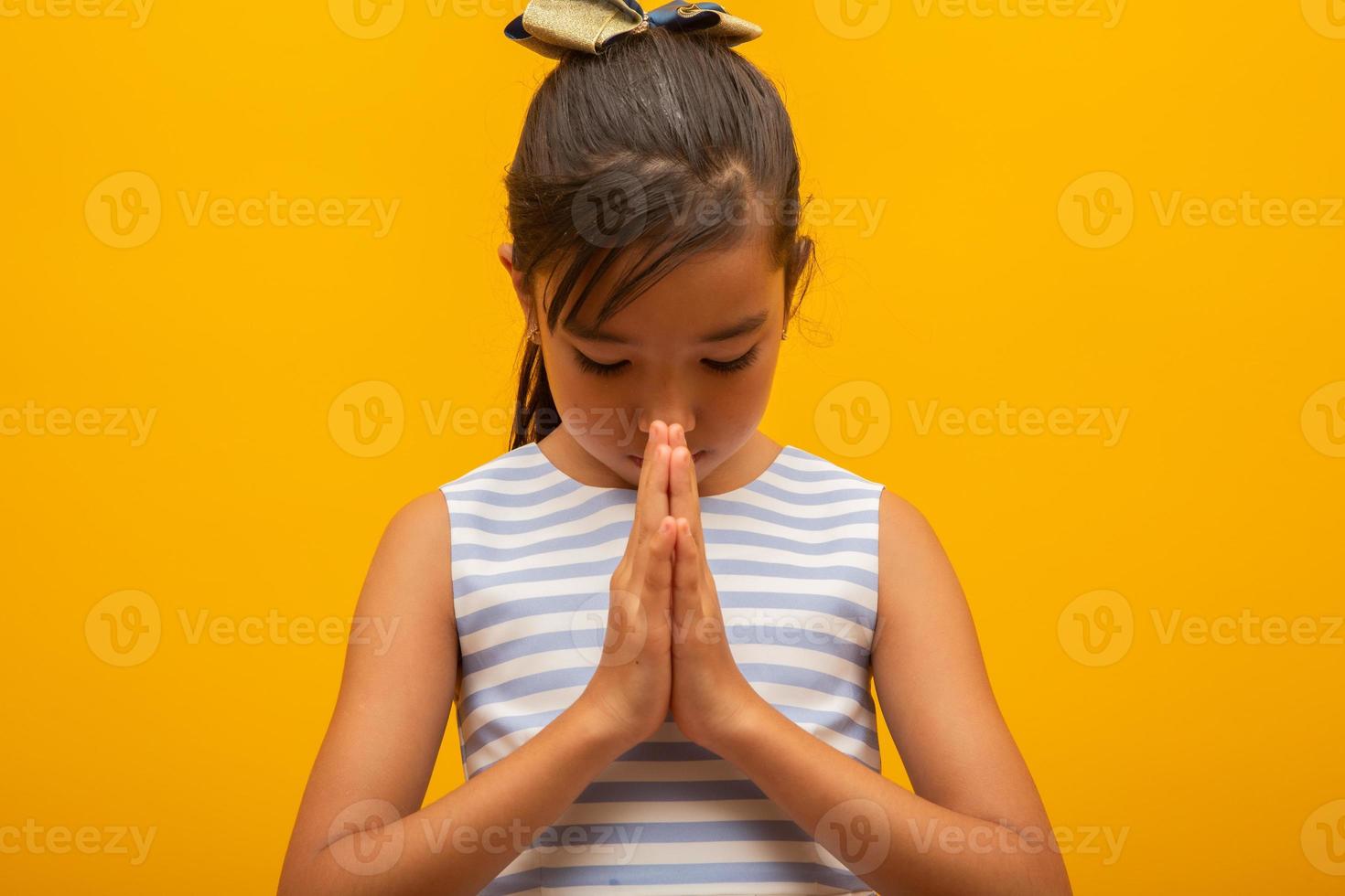 liten flicka ber på gul bakgrund. liten asiatisk flicka hand ber, händer vikta i bön koncept för tro, andlighet och religion. foto