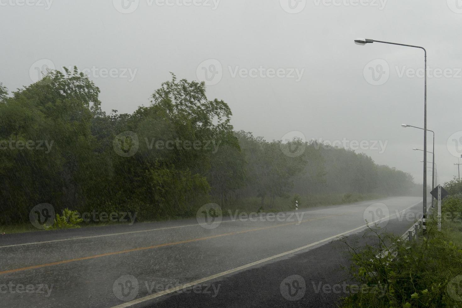 lång rak asfaltväg framåt i thailand. miljö av regnig tid. och bakgrundsträd och ljusstolpe. under den stormiga himlen. foto