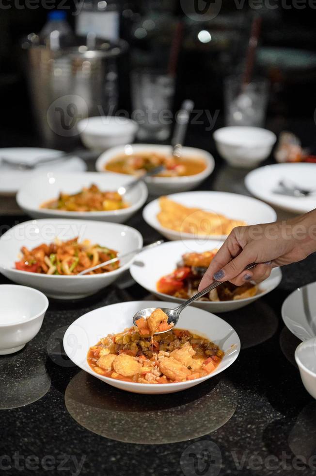 hand med sked scoop stekt tofu och olika thailändsk mat på matbordet foto