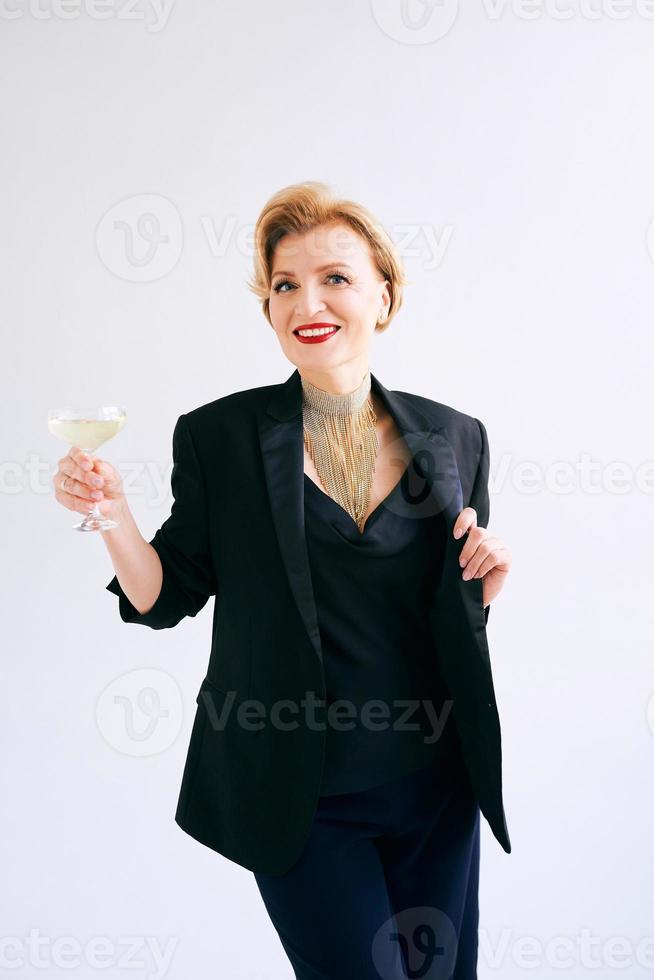 mogen elegant elegant kvinna i smoking med ett glas mousserande vin. fest, firande, anti ålder koncept foto