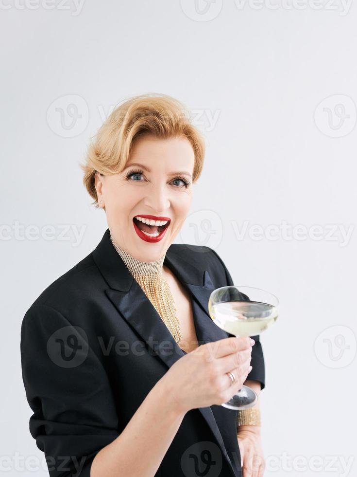 mogen elegant elegant kvinna i smoking med ett glas mousserande vin. fest, firande, anti ålder koncept foto