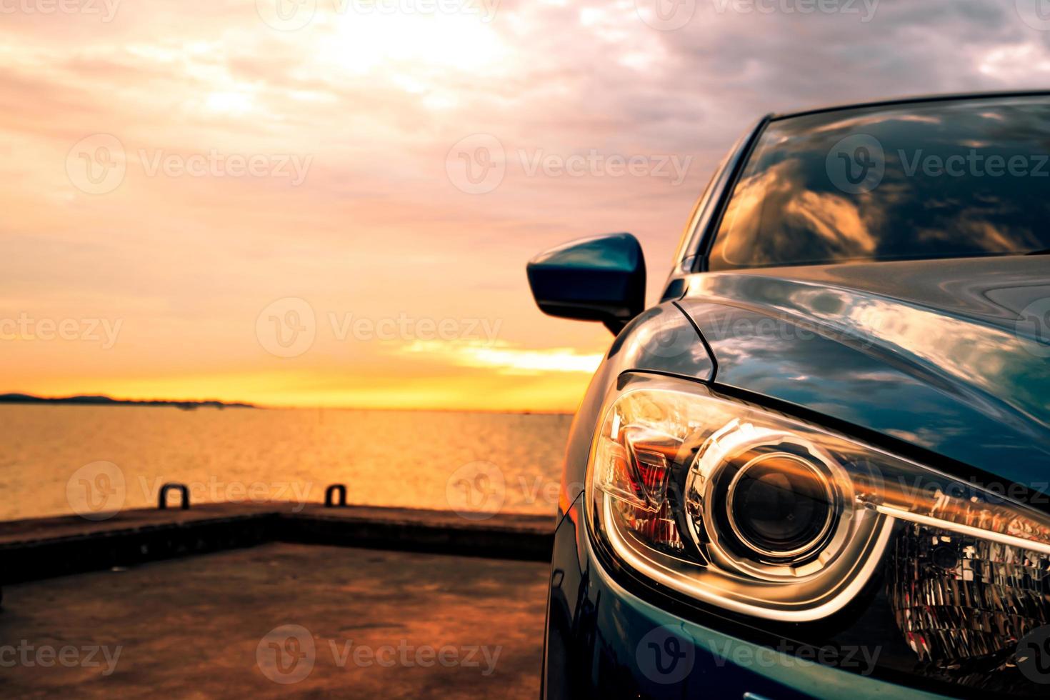blå kompakt suv-bil med sport och modern design parkerad på betongväg vid havet i solnedgången. miljövänlig teknik. affärsframgång koncept. foto