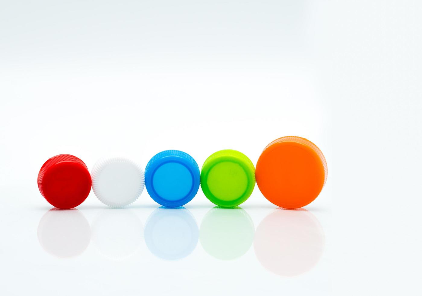 olika storlekar av vit, grön, röd, blå och orange färg runda plastskruvlock i en linje på vit bakgrund och kopieringsutrymme. foto